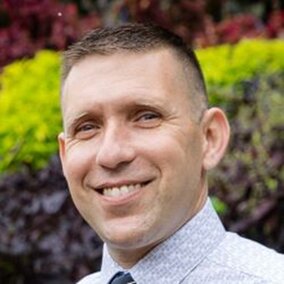 Dr. Seth Harris poses outside in front of foliage.