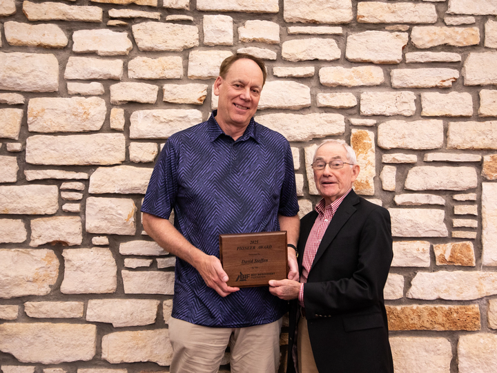 David Steffen poses in front of a stone wall next to a representative from the Beef Improvement Federation. Dr. Steffen is holding the 2025 Pioneer Award plaque.