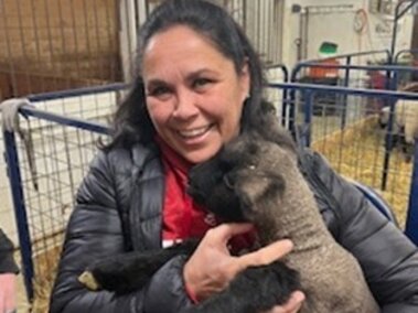Carrie Burkey holds a lamb. She is standing inside an area with pens of sheep.
