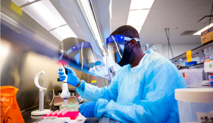 A lab technician, wearing protective equipment, is testing saliva samples for COVID-19.