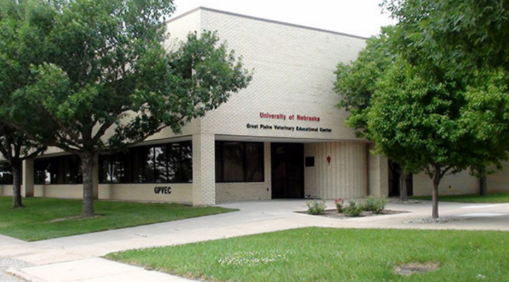 The exterior of the Great Plains Veterinary Educational Center. It's a light brown brick building, landscaped with trees and a small flowerbed near the entrance.