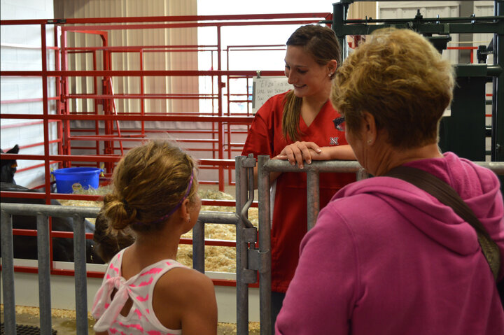 A SVMBS student speaks to a young girl and the adult with her about the animals in the State Fair birthing pavilion