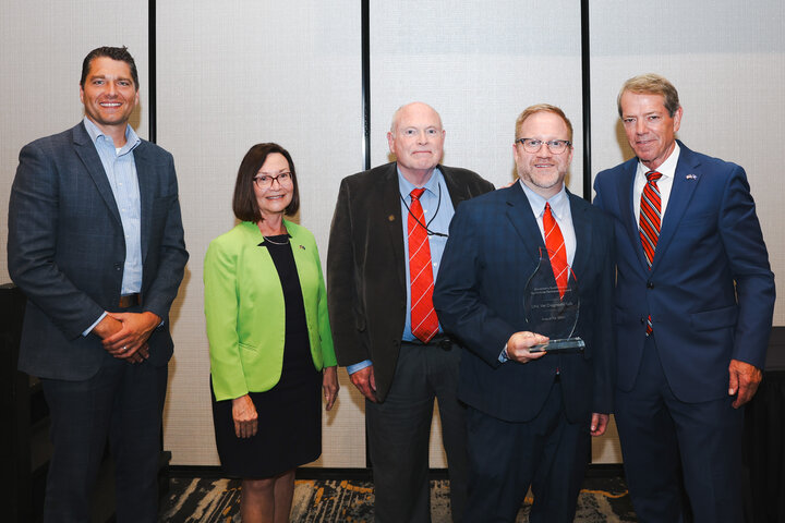 Governor Jim Pillen presents award to Dustin Loy, director of the NVDC. Scott McVey, director of the School of Veterinary Medicine and Biomedical Sciences stand next to them.