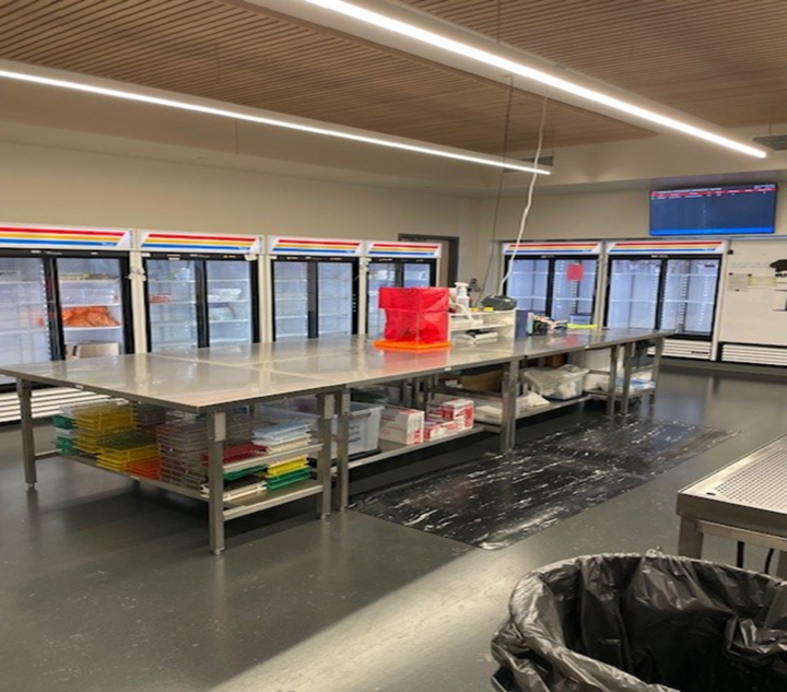 Interior of the sample receiving room. There are refrigerated coolers lining two walls and a large metal table in the center of the room.